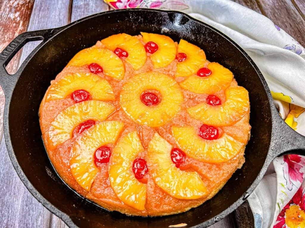 A pineapple upside-down cake with cherry toppings in a cast iron skillet.