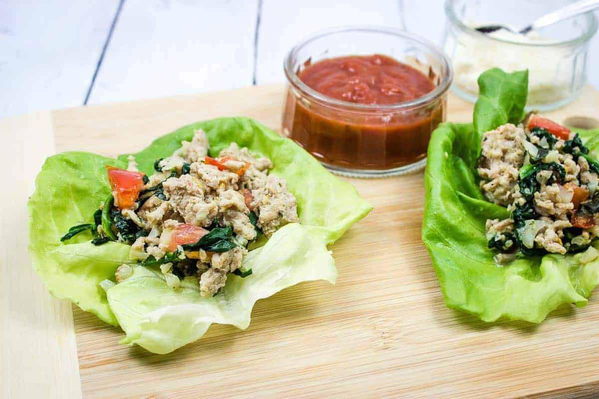 Two chicken parmesan lettuce wraps on a cutting board.