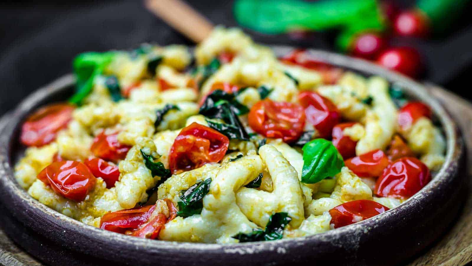 Brown plate with gnocci, tomatoes and basil leaves.