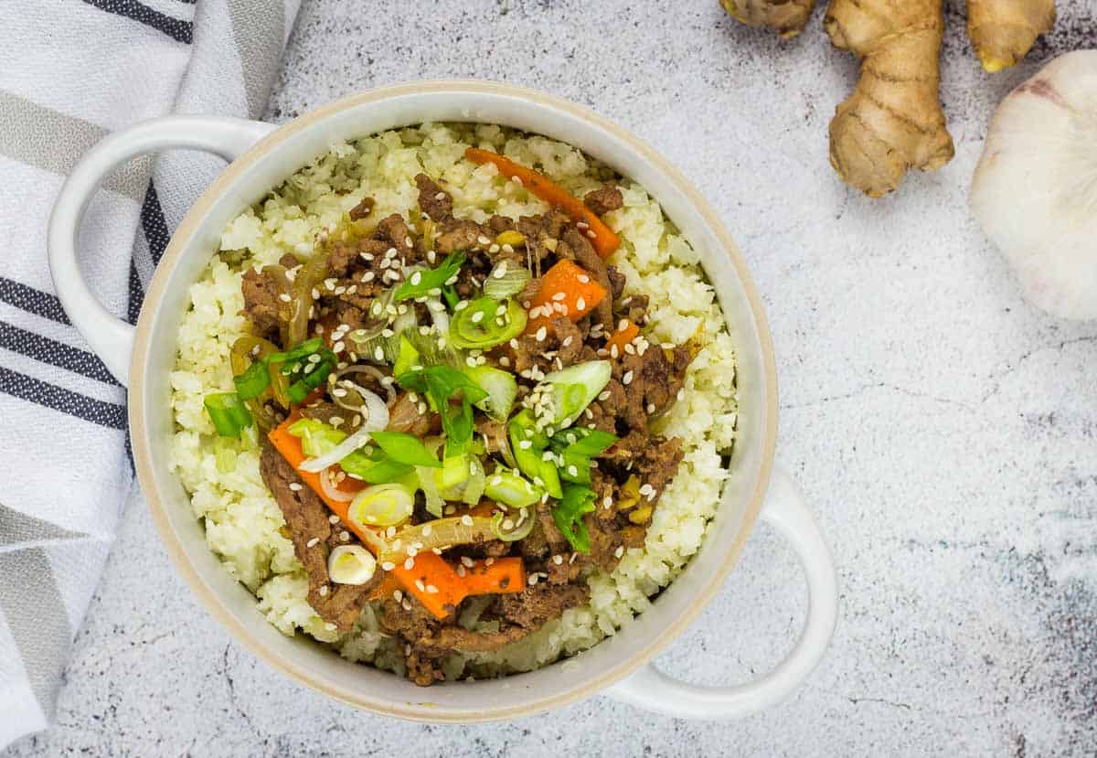 A top-down shot of Korean Beef Bowl with chopsticks, garlic, and ginger on the side.