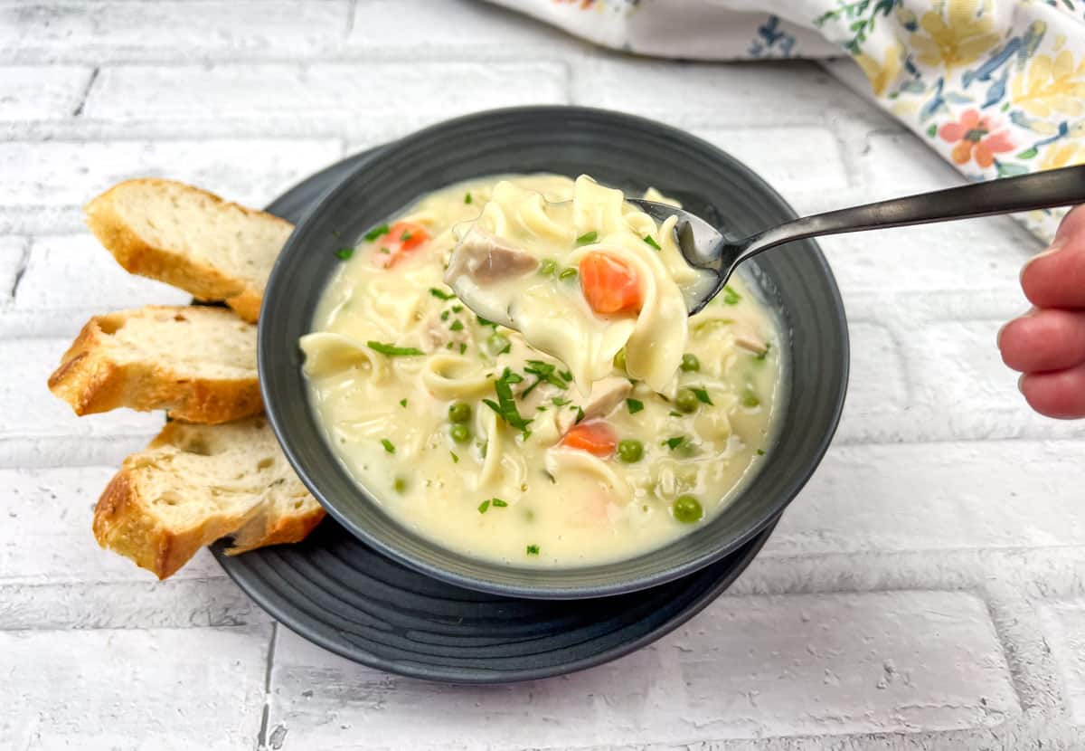 Creamy Turkey Noodle Soup on a bowl with bread slices on a plate.
