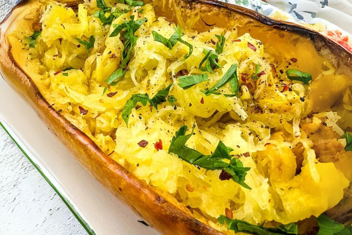 A baked spaghetti squash half filled with cooked strands, garnished with chopped parsley, black pepper, and red pepper flakes.