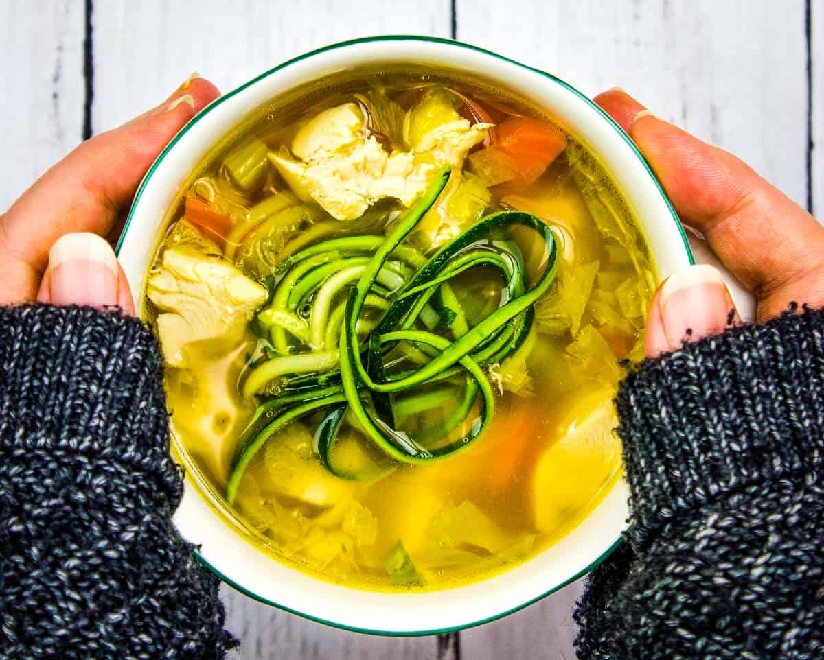 A hand holding a bowl of Chicken Zoodle Soup.