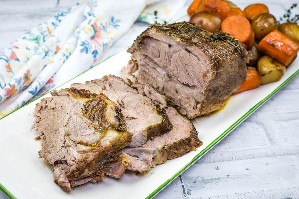 Slow Cooker Herb-Crusted Pork Roast with slices and roasted vegetables on a plate.