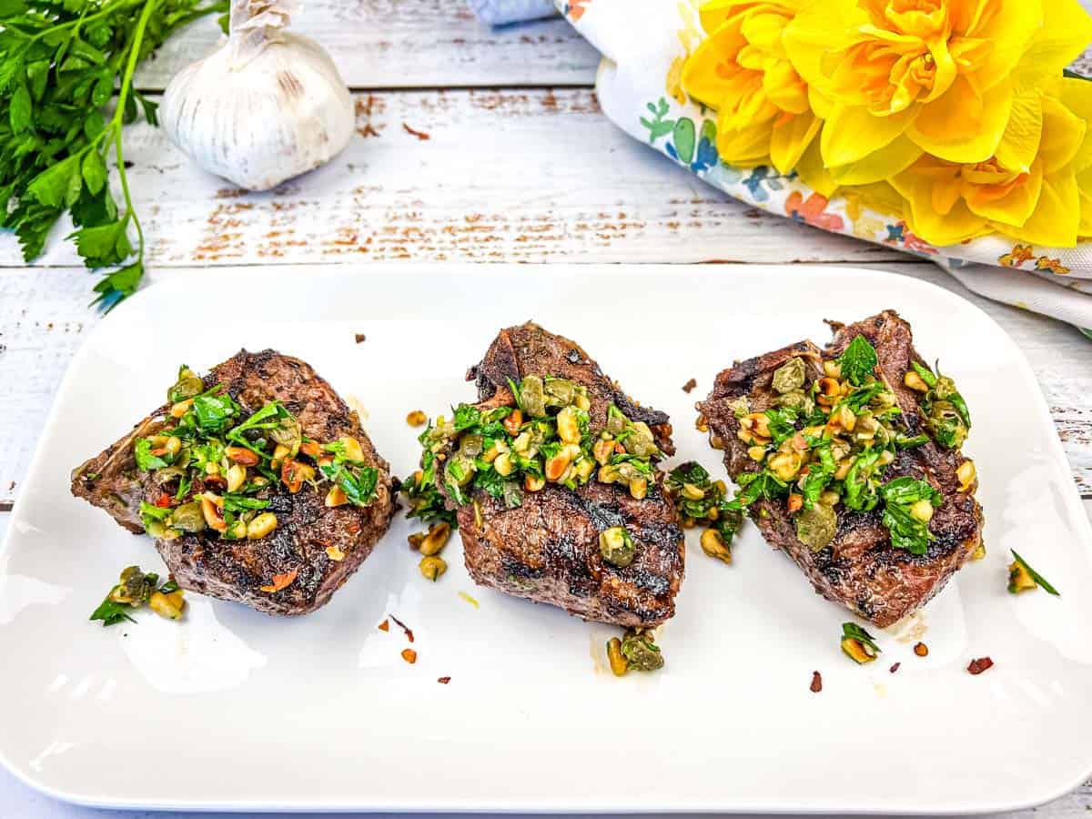Three Grill Mediterranean Lamb Chops topped with gremolata on a white plate.