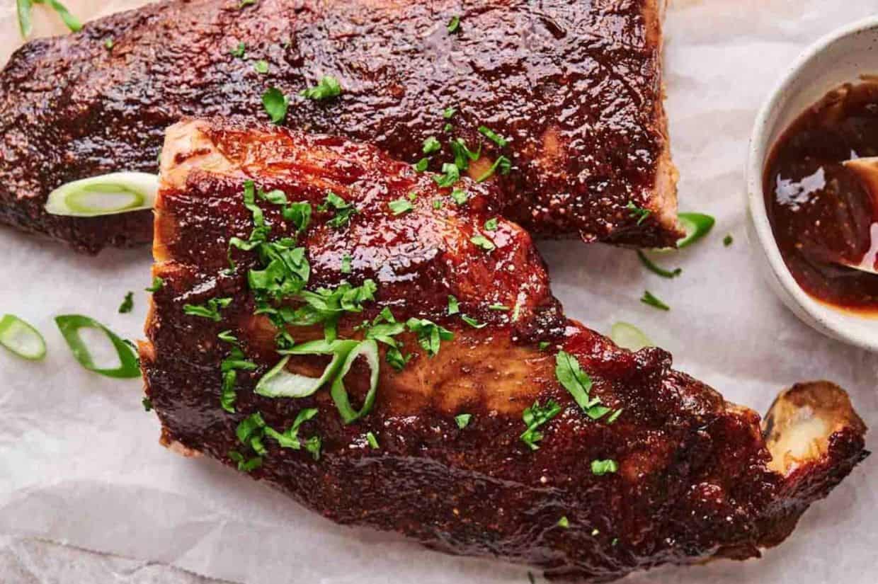 Oven-baked ribs with onion and garlic on top served on a white rectangular plate.