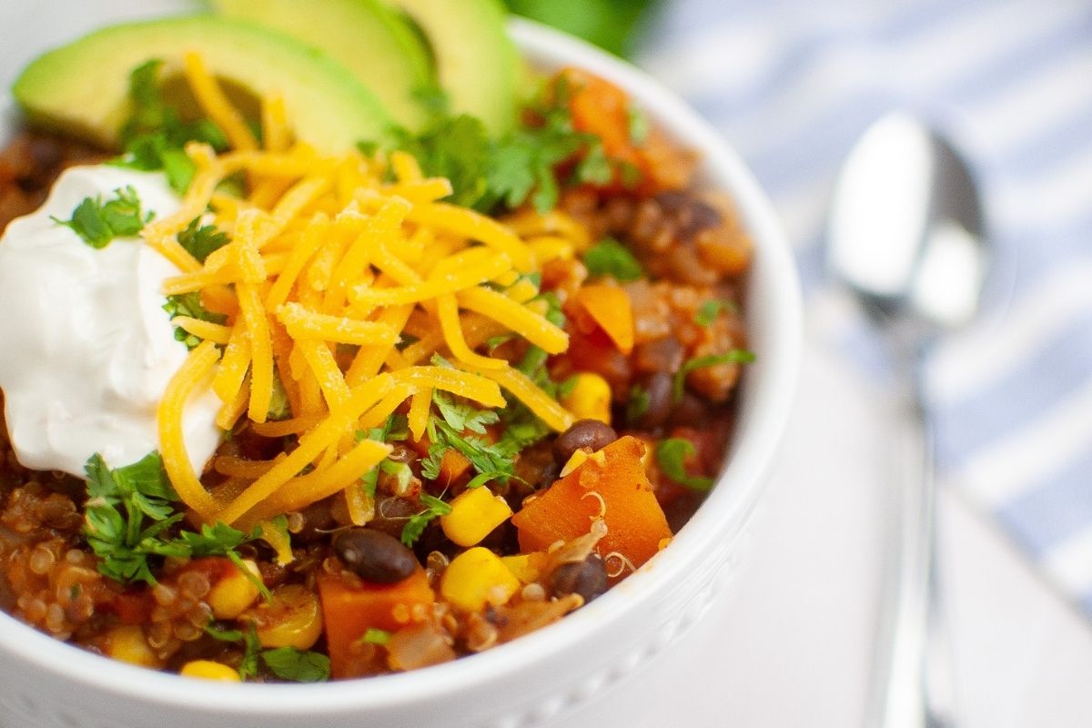 Sweet Potato Chili with Quinoa topped with avocado, cream, grated cheese, and cilantro.