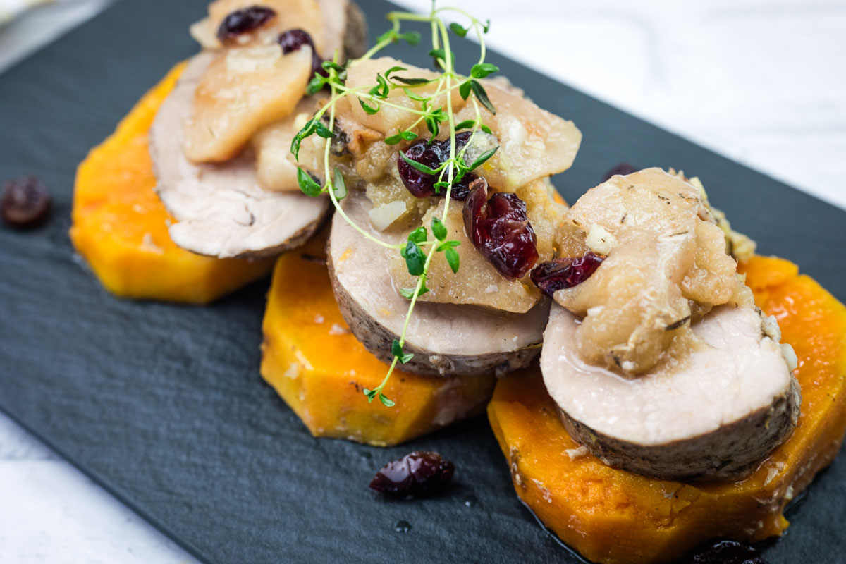 A serving of Slow Cooker Pork Tenderloin with Sweet Potatoes & Apples on a black platter.