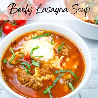 Bowl of beefy lasagna soup topped with herbs and cheese. Cherry tomatoes are visible in the background. Text at the top reads "Beefy Lasagna Soup.