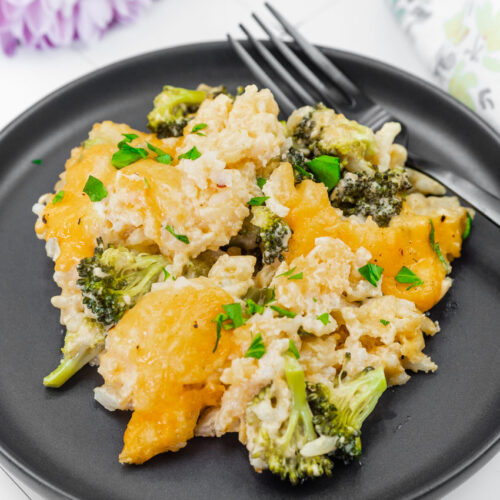 A plate of cheesy Broccoli Rice Casserole with No Canned Soup garnished with chopped herbs, served with a fork on a black plate.
