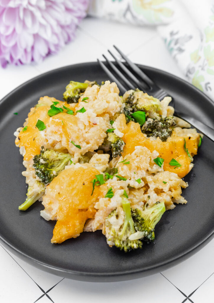 A plate of cheesy Broccoli Rice Casserole with No Canned Soup garnished with chopped herbs, served with a fork on a black plate.