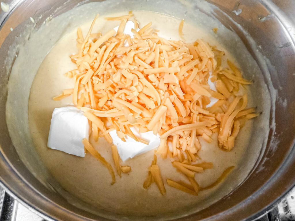 A pot of cheese sauce with shredded cheddar and cream cheese on top.