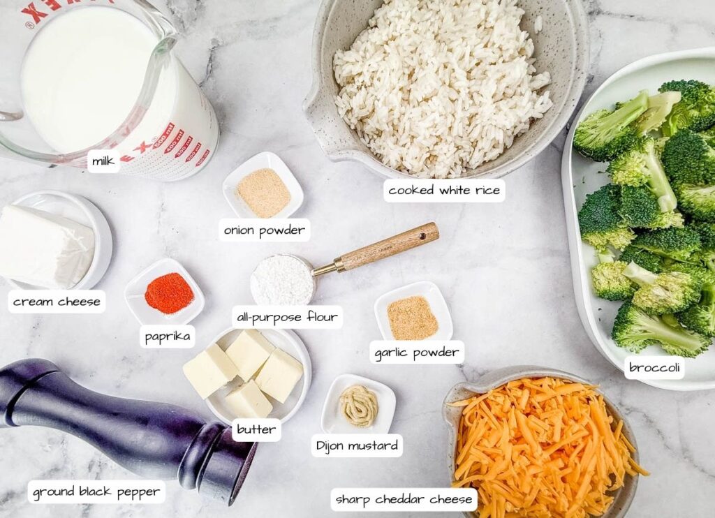 Ingredients for Broccoli Rice Casserole with No Canned Soup on a marble surface: milk, cooked rice, broccoli, cream cheese, butter, sharp cheddar, onion powder, garlic powder, paprika, flour, Dijon mustard, pepper.