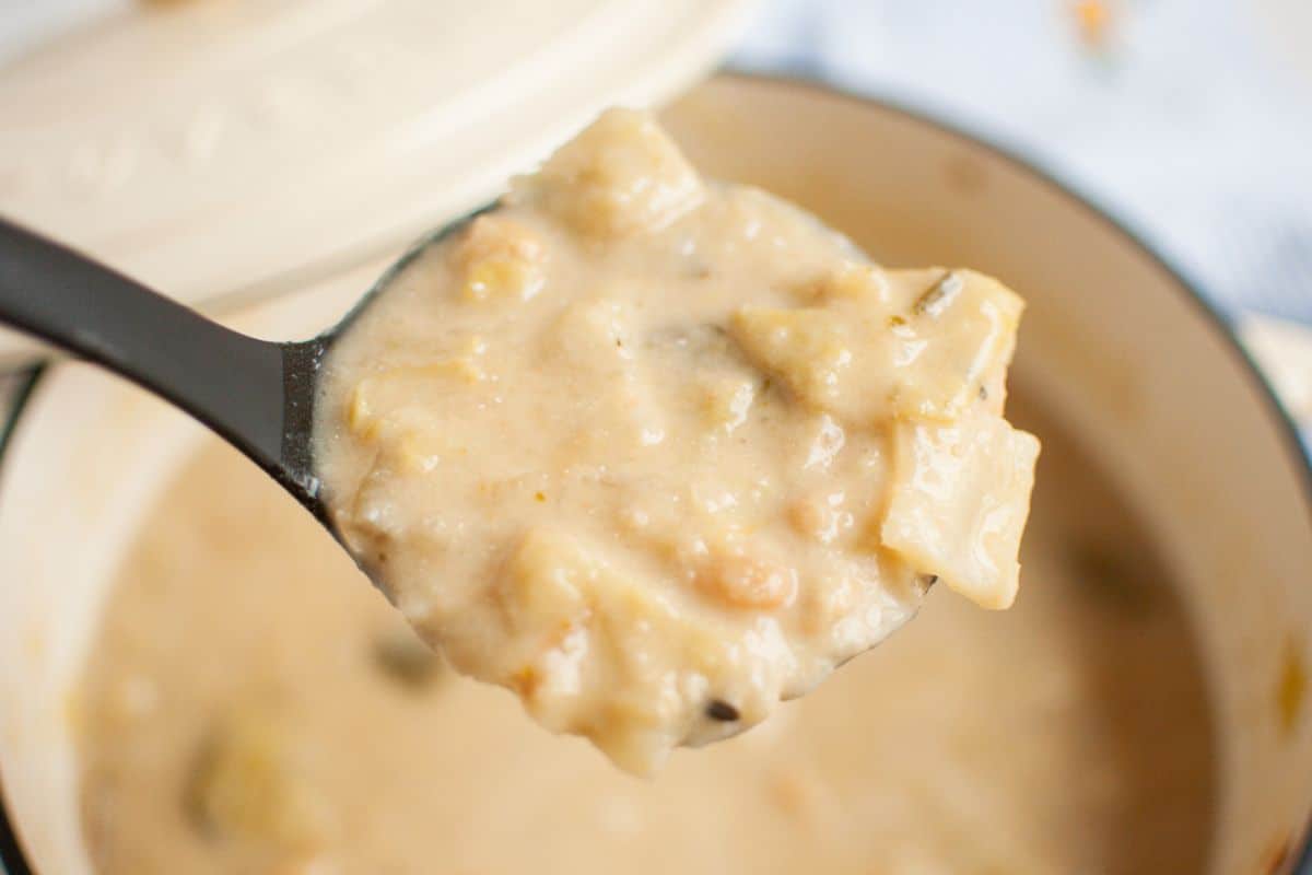 Close-up of a ladle holding Cabbage and White Bean Soup, above a pot filled with the same soup.