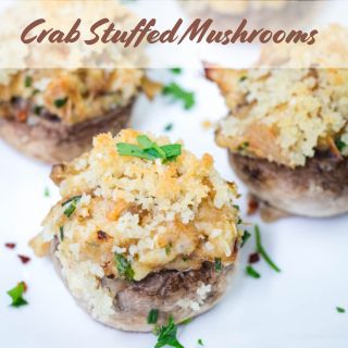 Crab stuffed mushrooms topped with breadcrumbs and herbs on a white plate.