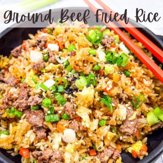 A bowl of ground beef fried rice with chopped green onions, carrots, and sesame seeds. Red chopsticks are placed on the side.
