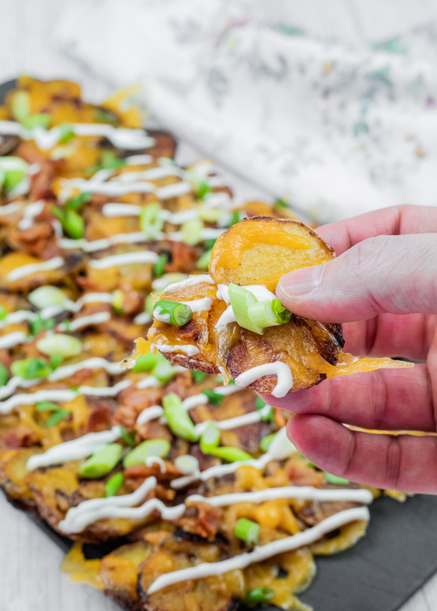 A hand holding an Irish nacho from a platter in the background.