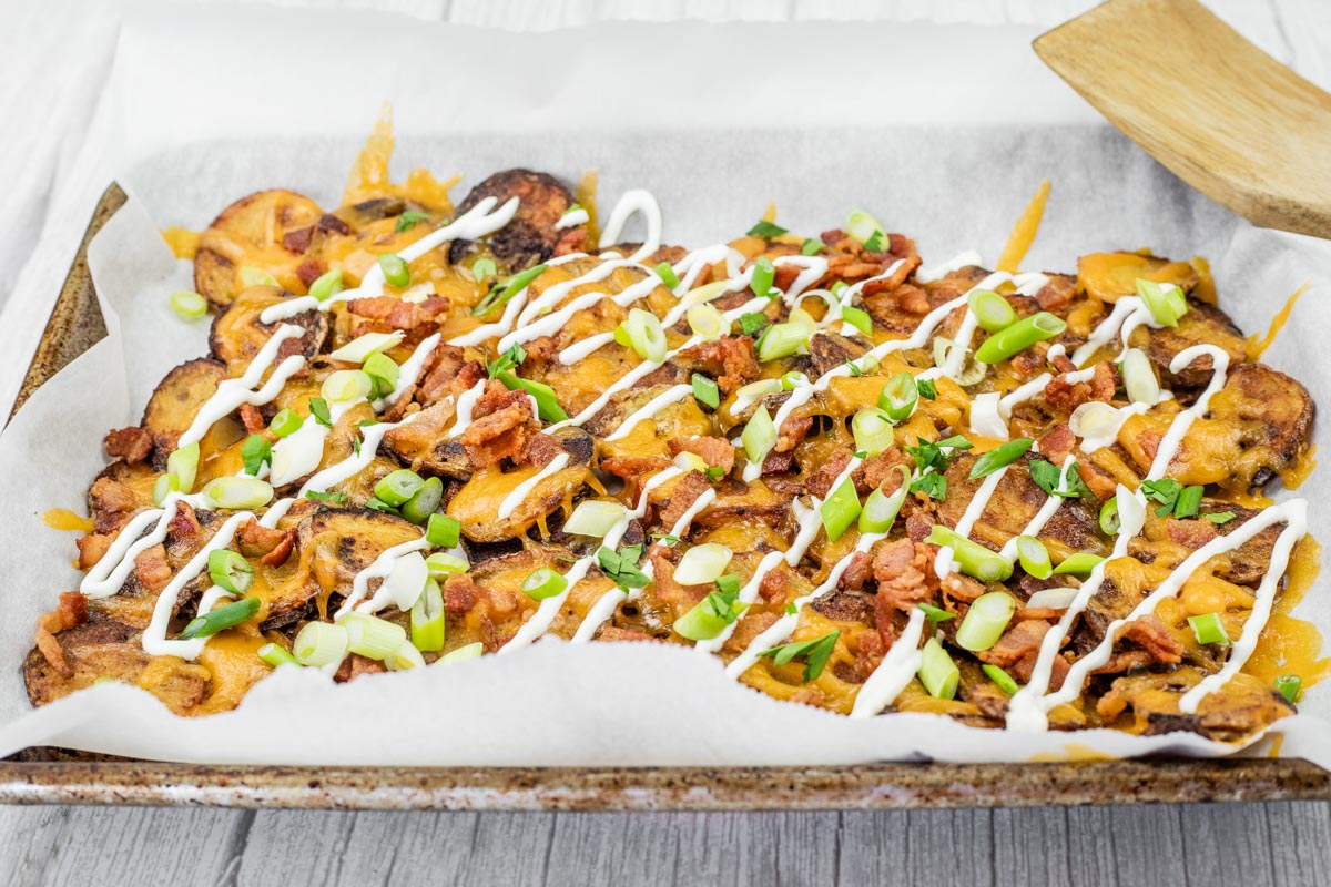 Tray of Irish nachos topped with green onions, bacon, cheese, and drizzled with sour cream.