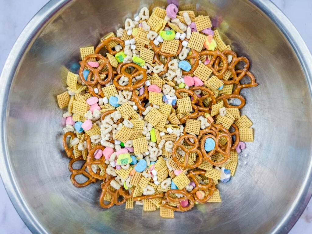 A large metal bowl filled with a snack mix of pretzels, cereal pieces, and colorful marshmallows.