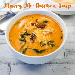A bowl of creamy chicken soup with spinach and sun-dried tomatoes, placed on a light-colored tile surface. Text overlay reads, "Marry Me Chicken Soup.