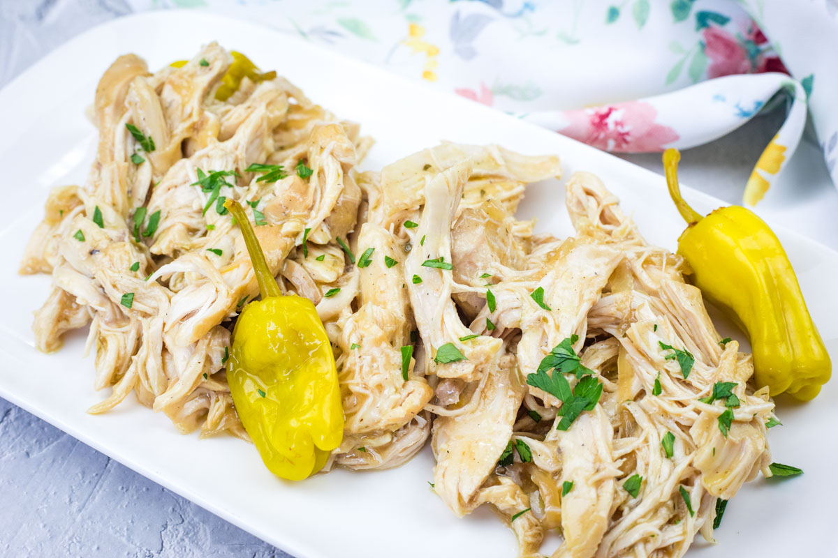 Mississippi Chicken - Slow Cooker with herbs and two yellow peppers on a white rectangular plate.
