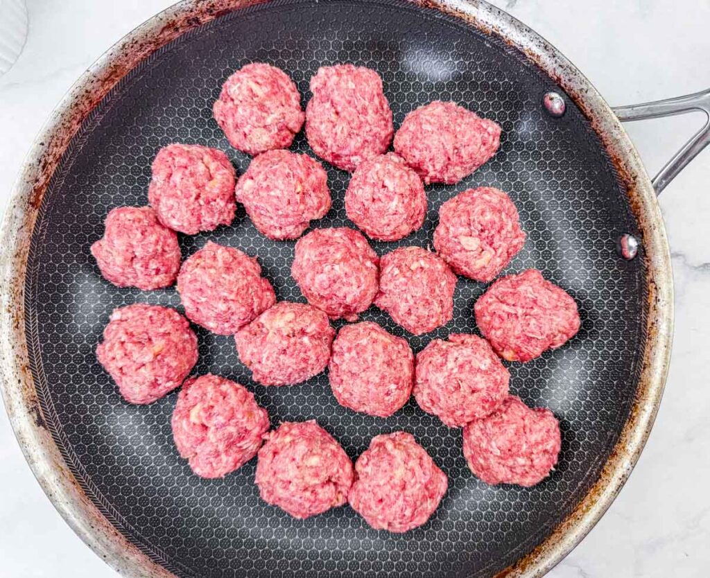 Raw meatballs arranged in a nonstick frying pan.