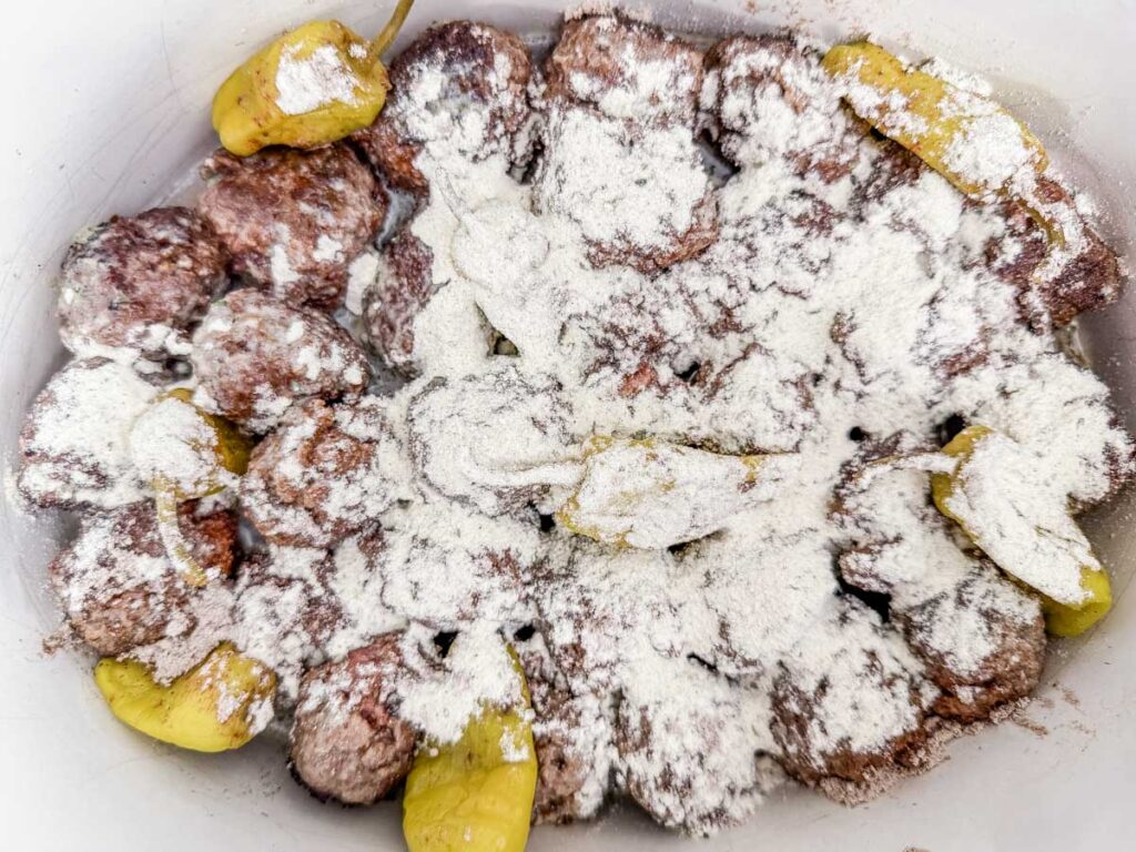 Meatballs coated with flour, surrounded by yellow pickled peppers.