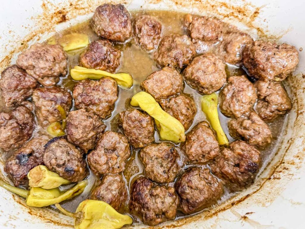 Cooked meatballs in a sauce with sliced yellow peppers in a white dish.