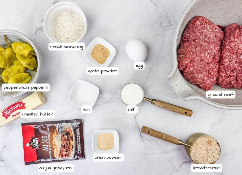 Ingredients for Slow Cooker Mississippi Meatballs on a white surface include ground beef, milk, breadcrumbs, egg, and various seasonings such as garlic powder, onion powder, and ranch seasoning, with butter and pepperoncini peppers.