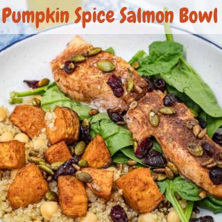 Salmon fillets with pumpkin spice seasoning on a bed of spinach, quinoa, roasted sweet potatoes, cranberries, chickpeas, and pumpkin seeds. Text reads "Pumpkin Spice Salmon Bowl.