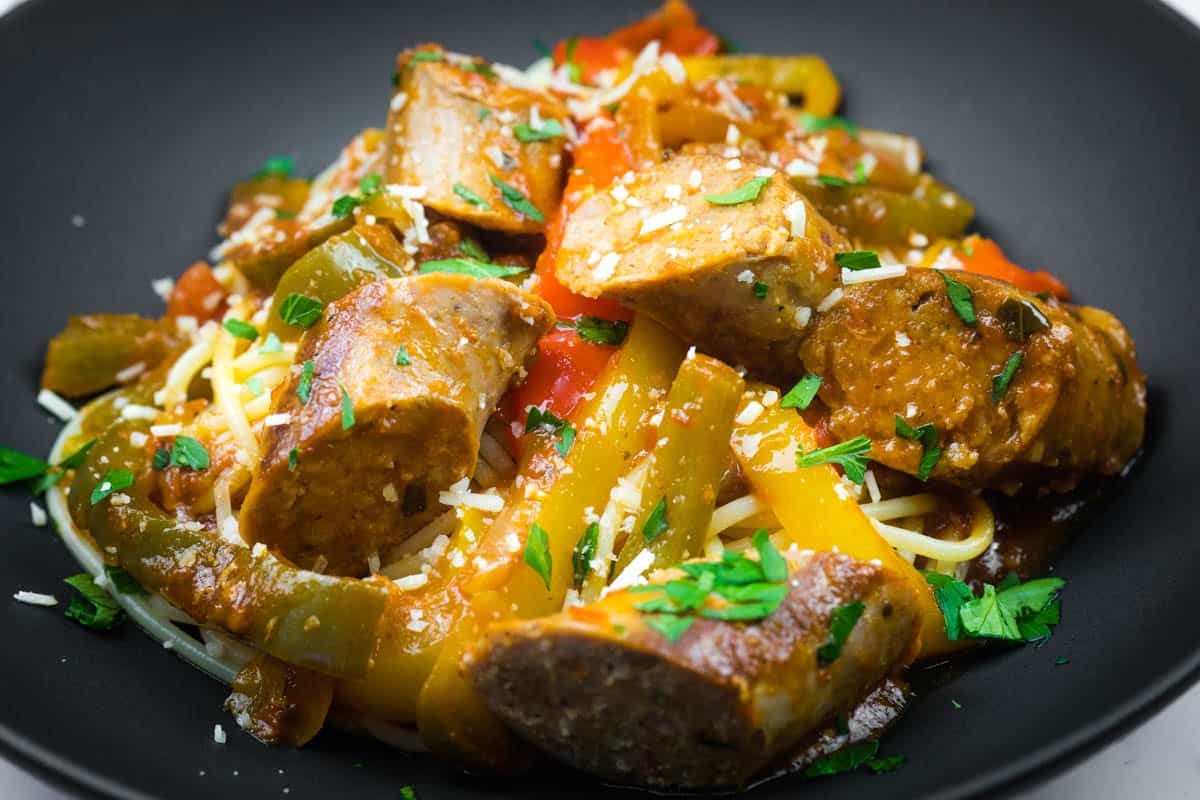 Slow cooker sausage and peppers garnished with grated cheese and chopped parsley.