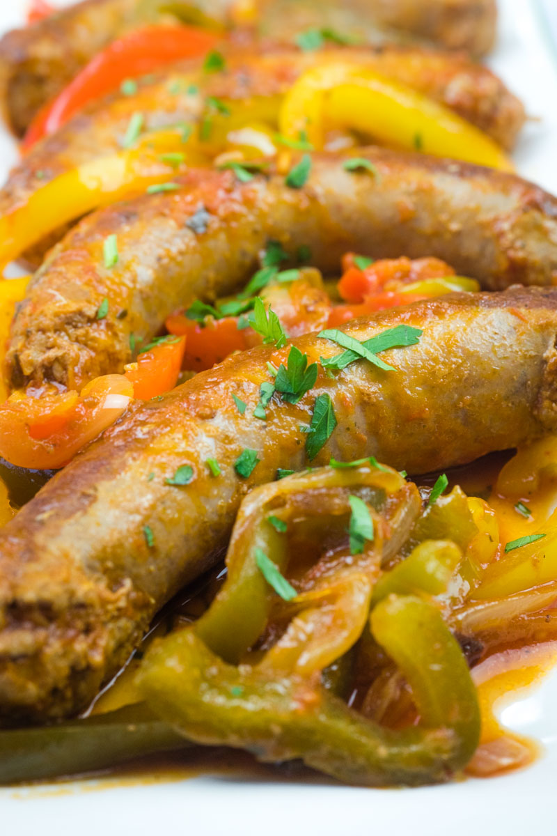 Plate of grilled sausages served with sautéed red, yellow, and green bell peppers, garnished with chopped herbs.