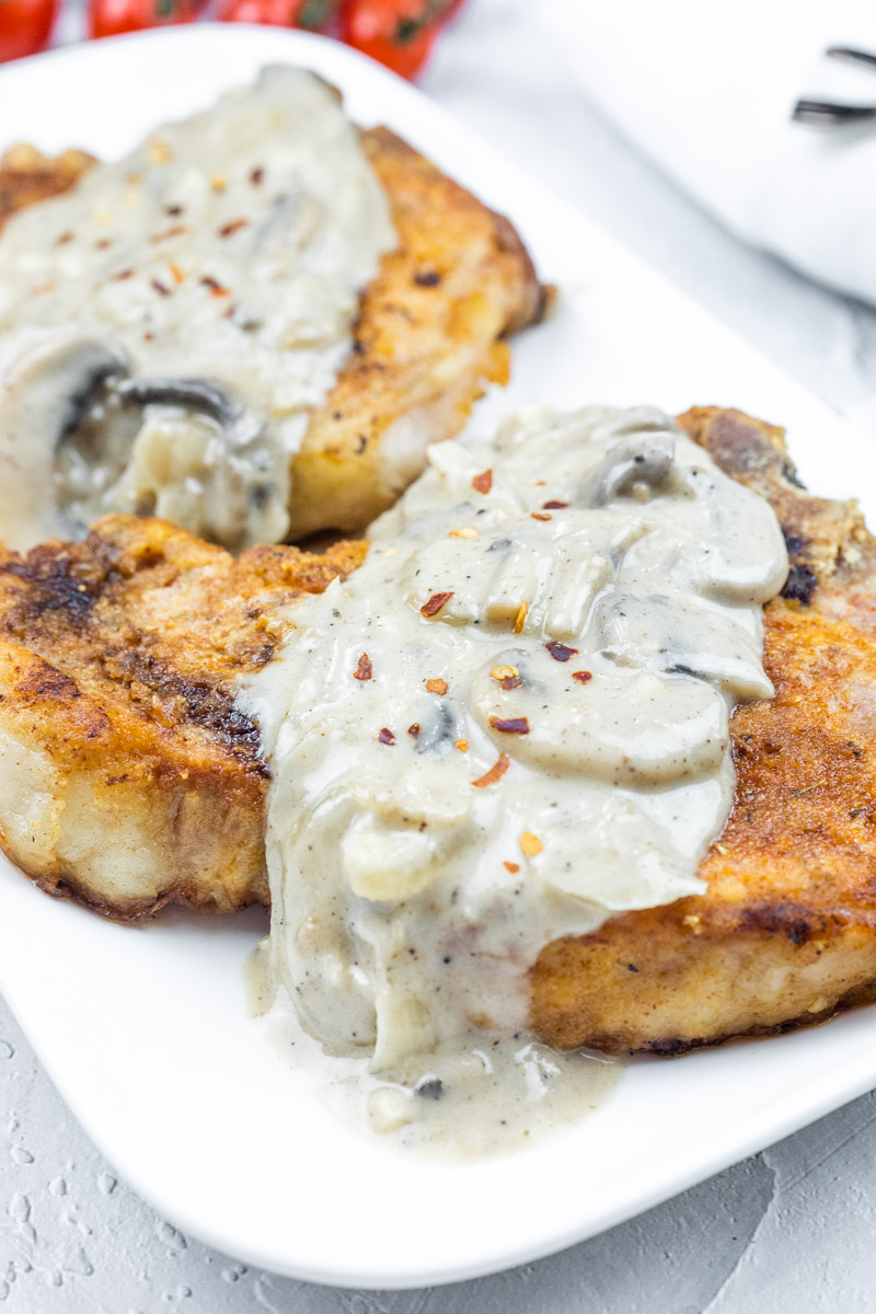 Two Smothered Pork Chops topped with creamy mushroom sauce on a white plate.