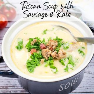 A bowl of Tuscan soup with sausage topped with kale and pancetta pieces in a black soup bowl.