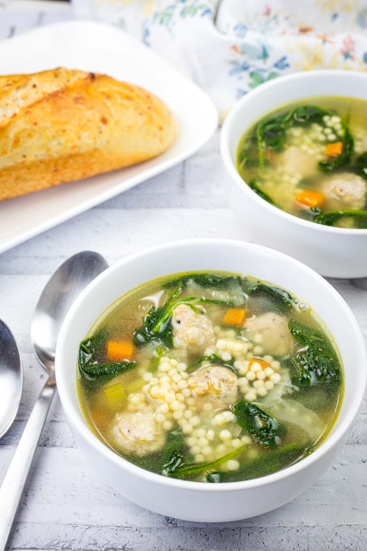 Two bowls of Italian Wedding Soup beside the plate of bread.