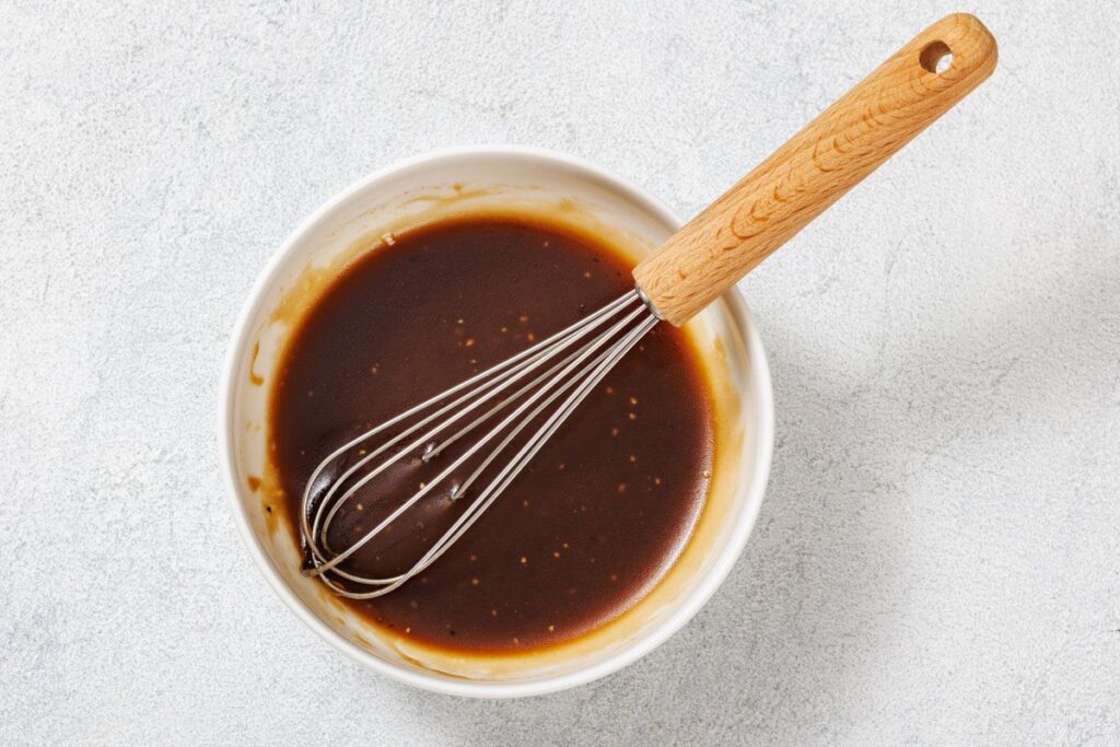 A whisk in a white bowl containing a brown liquid mixture.
