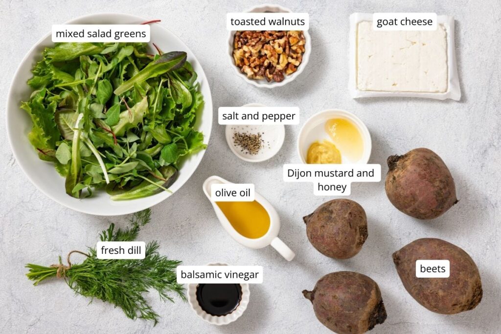 Ingredients on a table: mixed salad greens, goat cheese, toasted walnuts, fresh dill, beets, balsamic vinegar, olive oil, salt and pepper, Dijon mustard and honey.