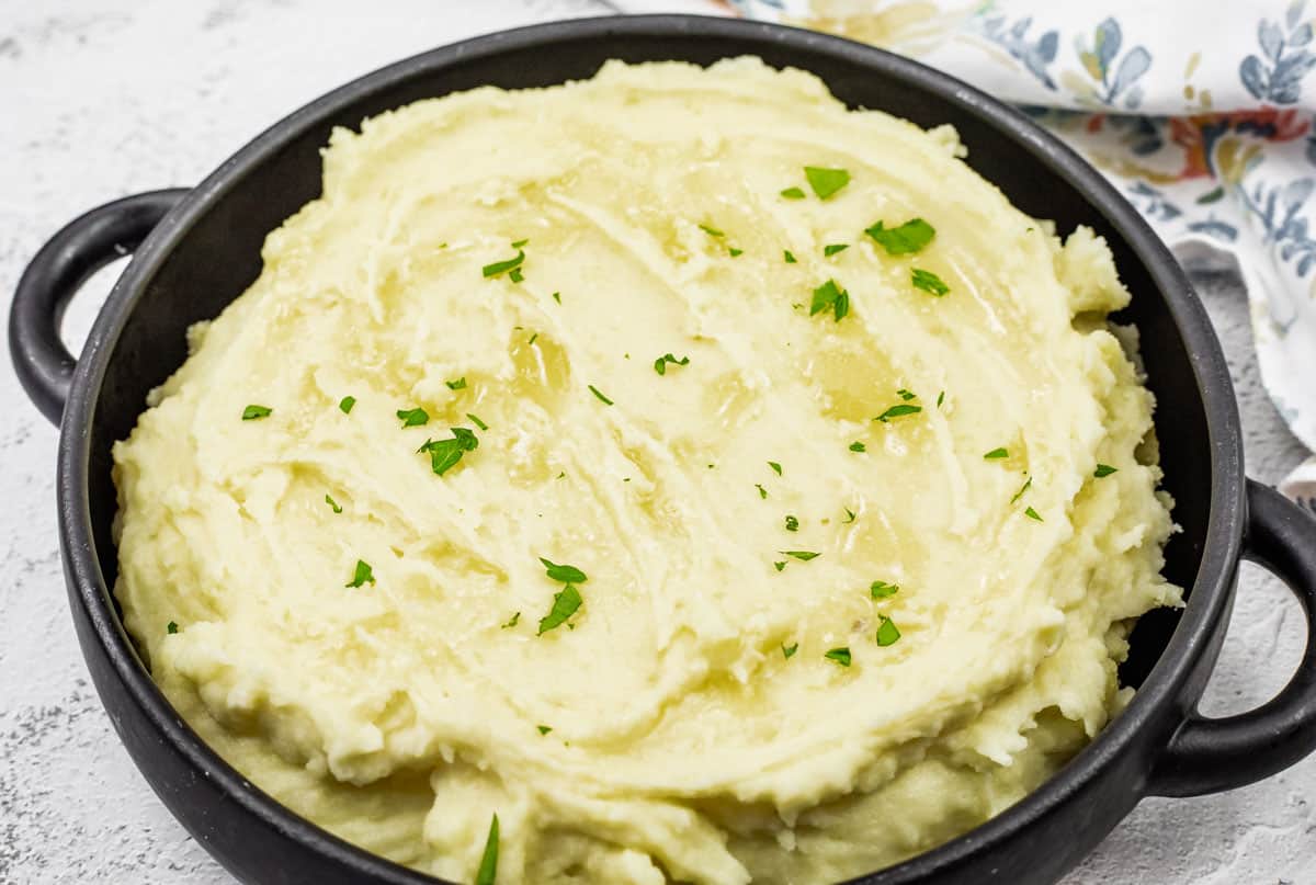 Mashed potatoes with cream cheese topped with melted butter and garnished with fresh parsley.