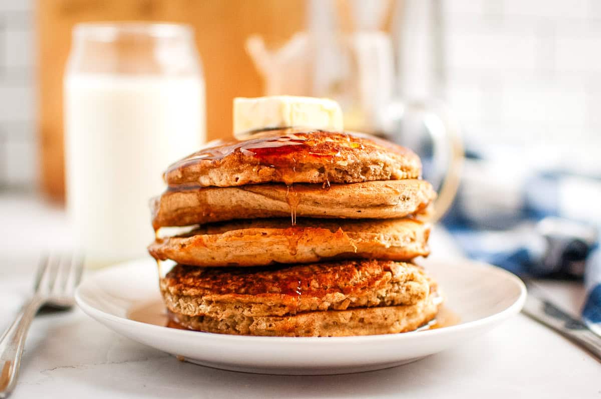 A stack of Buttermilk Oatmeal Pancakes with syrup and a pat of butter on top, served on a white plate.