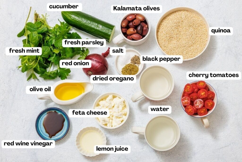 Ingredients for a Mediterranean quinoa salad laid out on a surface, including cucumber, Kalamata olives, quinoa, fresh herbs, olive oil, feta, cherry tomatoes, and seasonings.