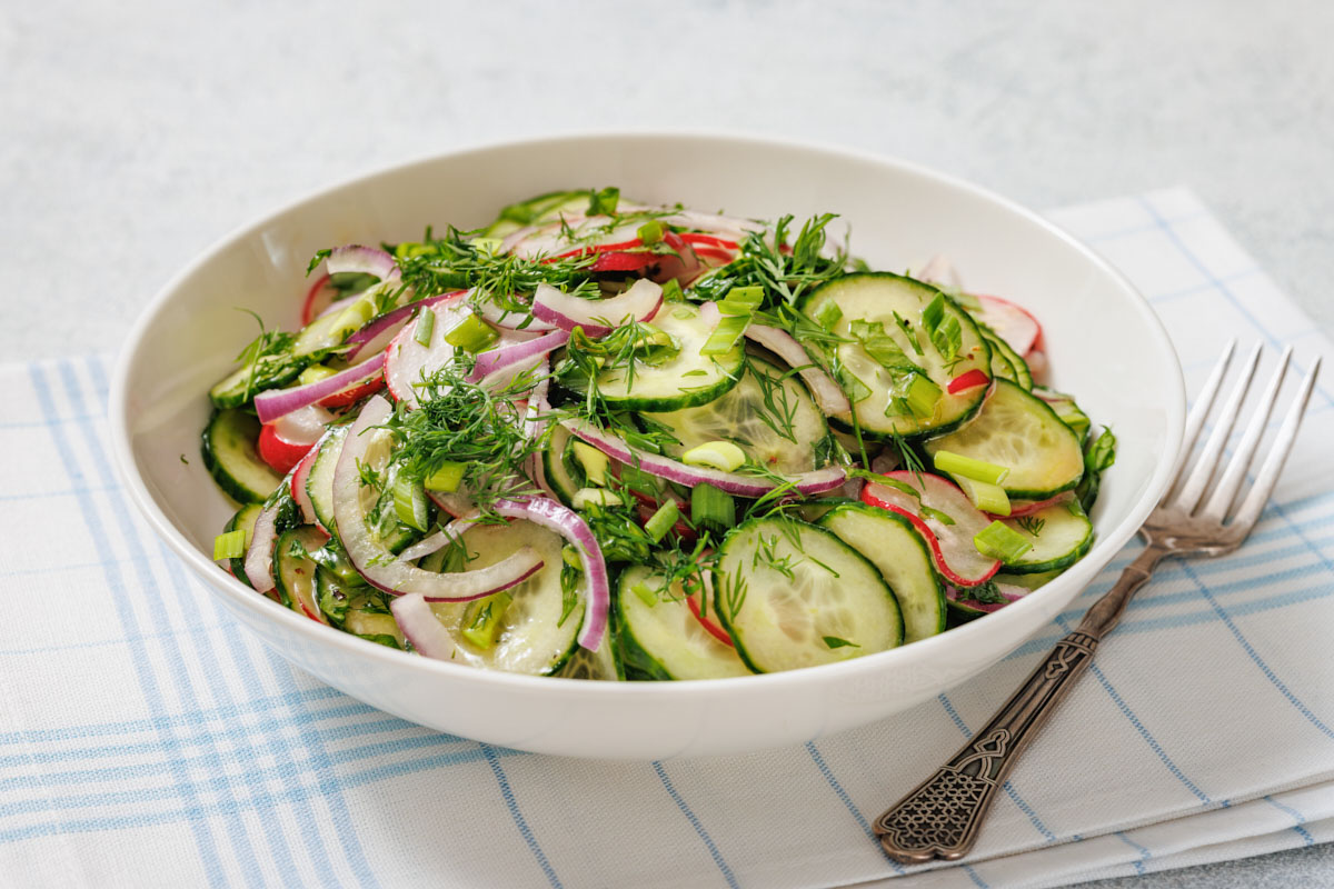 Bowl of Radish Salad with red onion, radishes, and fresh herbs on a plaid cloth, accompanied by a fork.