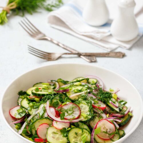 A bowl of Radish Salad with radishes, red onions, and fresh herbs. Two forks, napkins, salt, and pepper shakers are in the background.