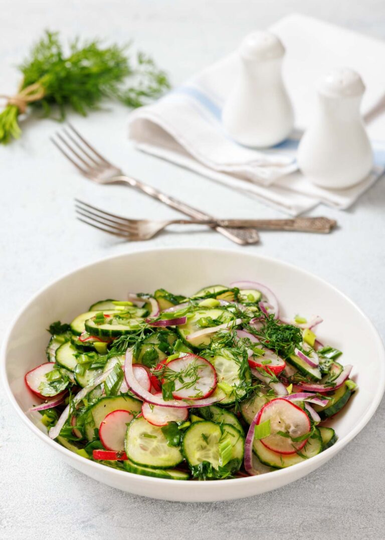 A bowl of Radish Salad with radishes, red onions, and fresh herbs. Two forks, napkins, salt, and pepper shakers are in the background.