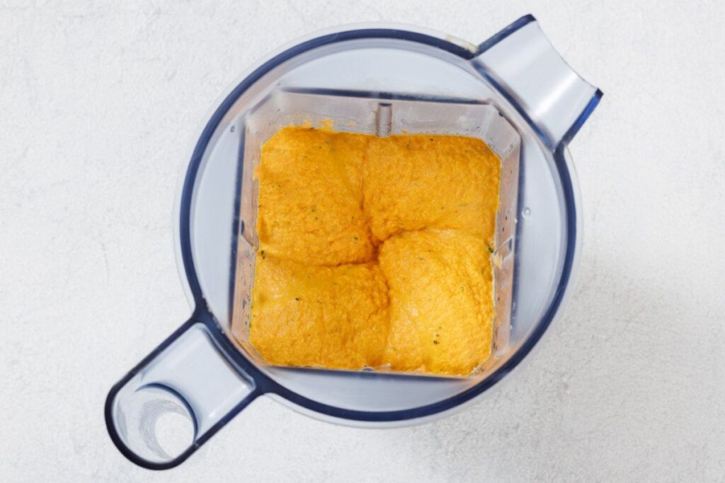 Blender jug containing a smooth orange mixture, viewed from above on a light gray surface.