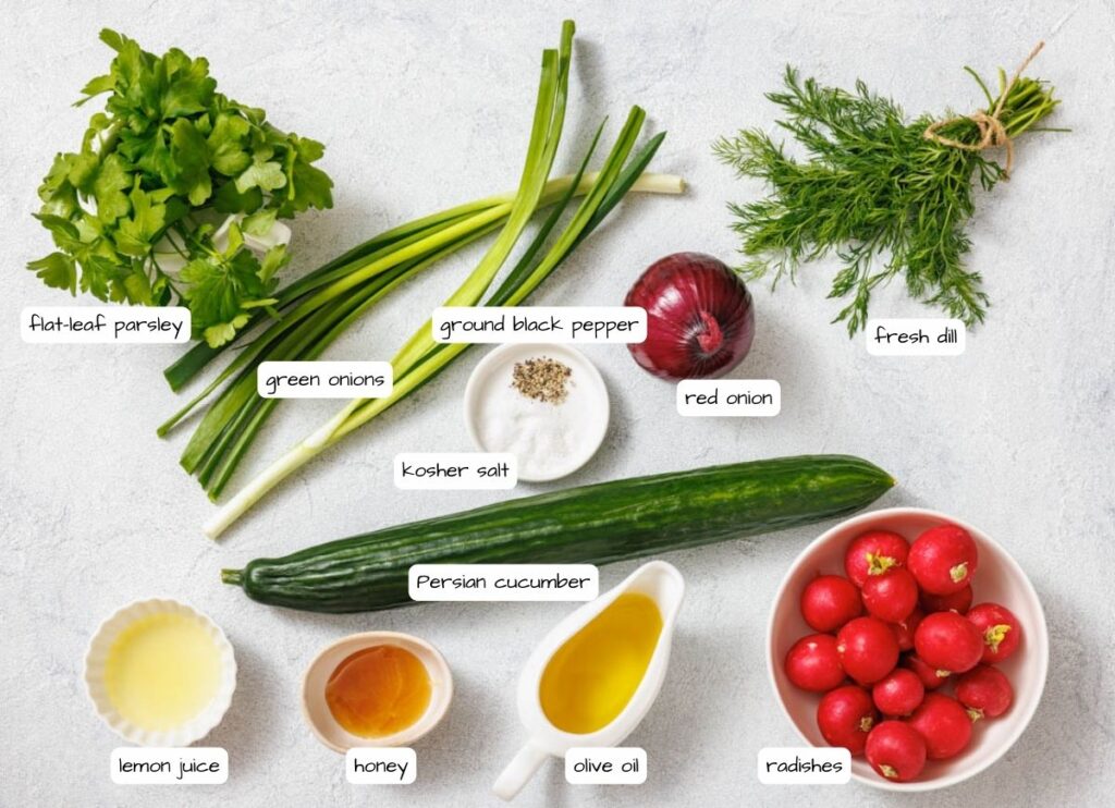 Ingredients laid out for a salad, including flat-leaf parsley, green onions, ground black pepper, red onion, fresh dill, Persian cucumber, kosher salt, lemon juice, honey, olive oil, and radishes.