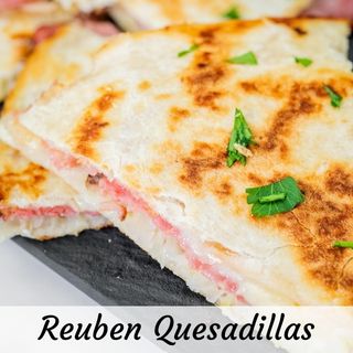 Close-up of a quesadilla with melted cheese and ham on a slate board, garnished with chopped parsley.
