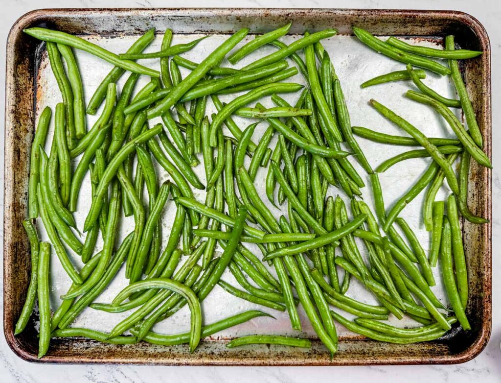 A baking sheet filled with raw green beans spread out evenly.