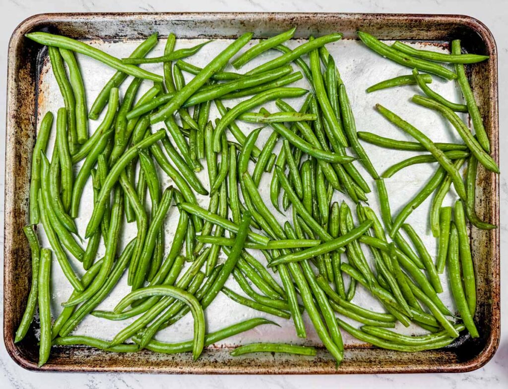 Fresh green beans spread across a metal baking sheet on a white surface.