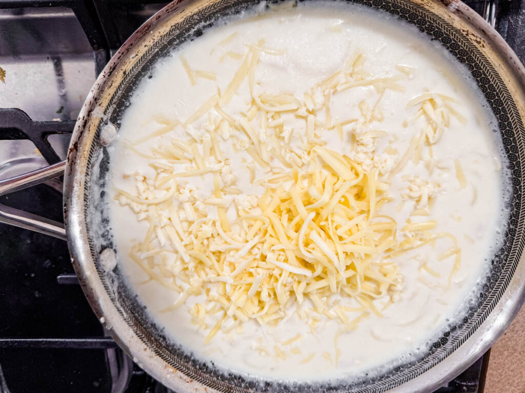 Cheese melting in a frying pan on a stovetop, surrounded by a creamy white sauce.