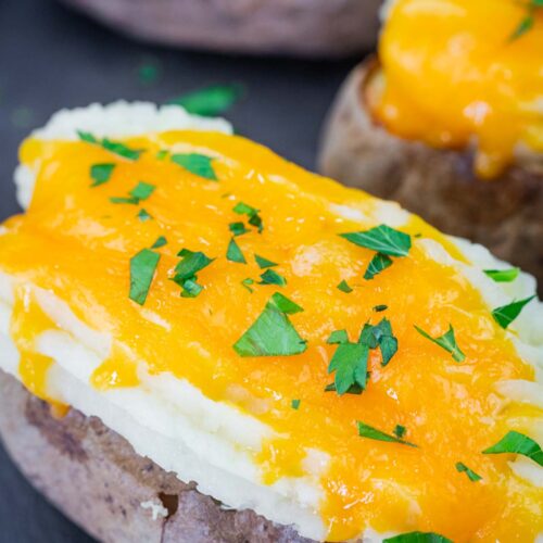 Close-up of Shepherd’s Pie Baked Potatoes topped with melted cheddar cheese and chopped parsley.